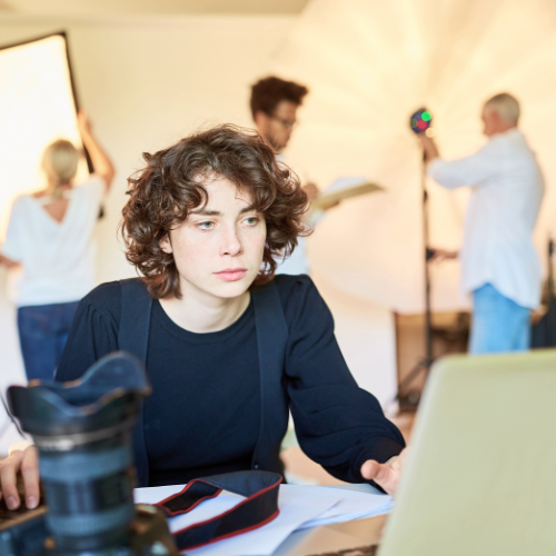 Person working on a laptop in a photo studio, with camera gear on the table.