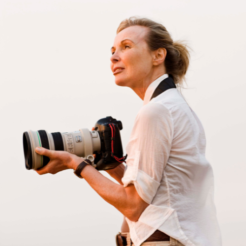 Woman holding a professional camera and looking off into the distance.